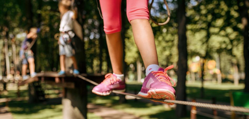 Close up of a child's legs wearing pink trainers walking a tightrope in the garden