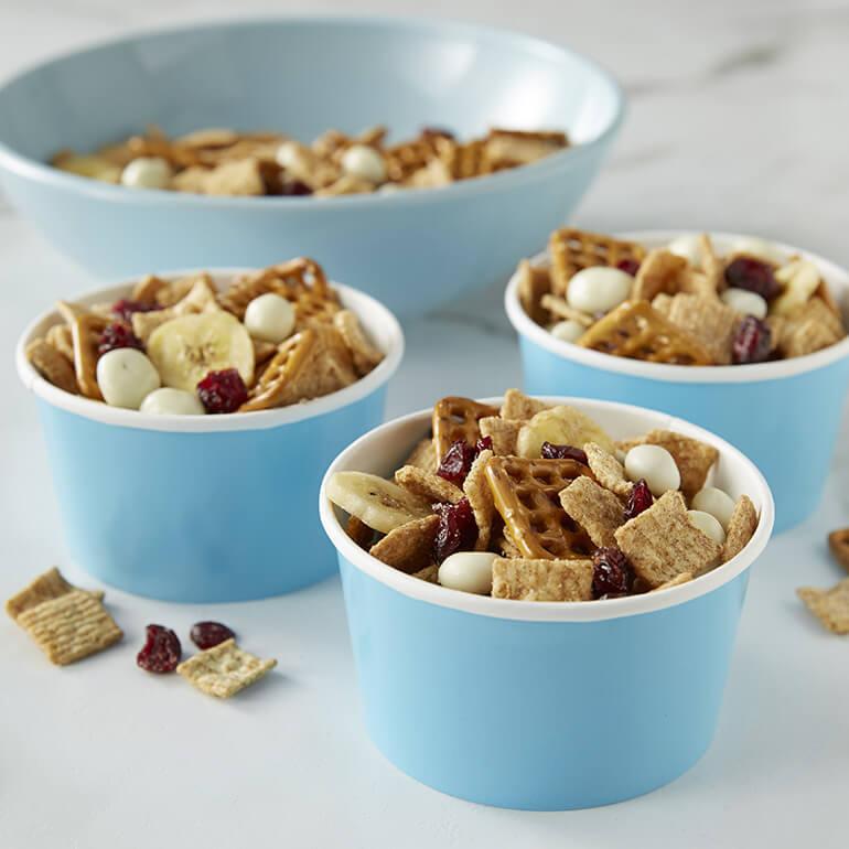 Fruit & Cinnamon Snack Mix filling three separate cardboard cups and a bowl behind them.