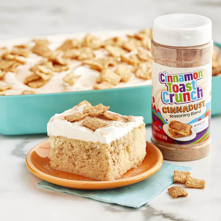 A slice of Cinnamon Toast Crunch™ Cinnadust™ Tres Leches Cake on a plate with a jar of Cinnadust™ beside it.