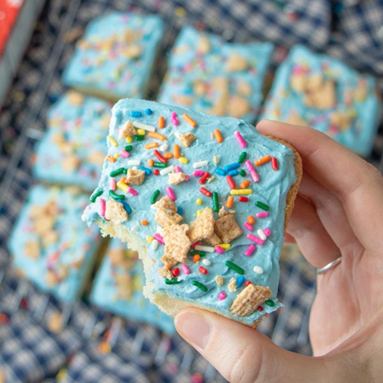 A hand holding a Sugar Cookie Toast Crunch™ Holiday Bar above the Sugar Cookie cereal box.